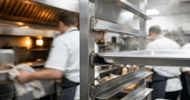 Close-up of stainless steel pan rack with baking tray sliding into heavy-duty kitchen runners.